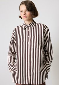 Chemise à rayures marron et crème avec un col, une poche poitrine simple et des manches longues. Fabriquée dans un tissu lisse avec une coupe décontractée.