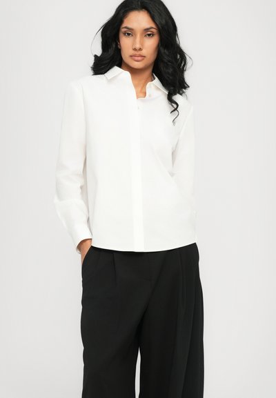 Cămașă albă cu guler clasic și mânecă lungă, combinată cu pantaloni negri cu talie înaltă, având un design elegant și curat.