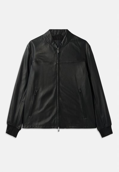 Chaqueta de cuero negra con cuello alto, cierre frontal de cremallera y dos bolsillos laterales con cremallera. Presenta una textura suave y un corte entallado.