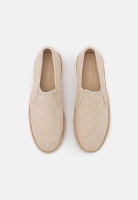 Scarpe slip-on beige realizzate in tessuto testurizzato con suola in corda di juta. Presentano una punta rotonda e inserti elastici ai lati per indossarle facilmente.
