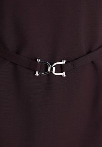 Tmavě hně dress z látky s kovovým sponou, elegantním designem a hladkou texturou, který zdůrazňuje minimalistické akcenty.