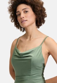 Zielona satynowa sukienka z cienkimi ramiączkami, dekoltem w kształcie czołgu i gładką fakturą. Dopasowana sylwetka podkreśla kształt ciała.