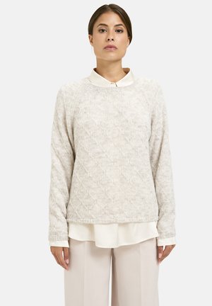 Helles beige gestricktes Sweatshirt mit strukturiertem Rautenmuster, Rundhalsausschnitt und langen Ärmeln, das über einem weißen Hemd mit Kragen getragen wird.