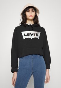 Črna Levi's kapuca s srebrnim logotipom, z kenguru žepom in nastavljivimi vrvicami. Kombinirano z visokim pasom modrimi kavbojkami.