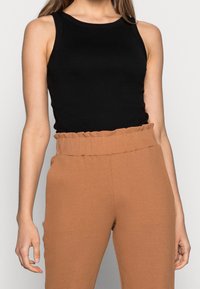 Svart ärmlös topp med en slät textur, kombinerad med högmidjade bruna ribbade byxor med en volangmidja.