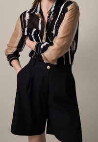 Skjorte med krave i sort, creme og brunstribet mønster; kombineret med højtaljede sorte shorts med knap og sidelommer.