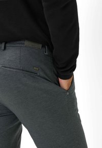 Pantaloni grigi dalla texture morbida con vestibilità slim, caratterizzati da dettagli sulle tasche posteriori e un sottile logo accentato sulla cintura.