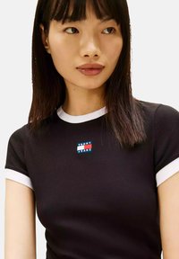 Černé krátké tričko s žebrovanou strukturou a bílým lemováním, na hrudi s modro-červeným obdélníkovým logem "TOMMY JEANS".