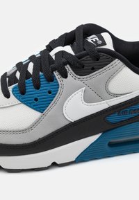 Nike Air Max-sneaker med grå och svarta material, blå accenter, mesh-textur och vit swoosh-logga på sidan. Svarta snören.