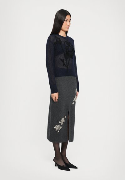 Pulôver de malha azul-marinho com painéis transparentes e bordado floral preto, combinado com uma saia cinza com aplique floral e uma fenda na frente.