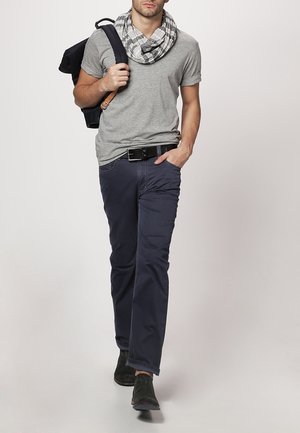 Szary t-shirt, granatowe spodnie i czarny szal w biało-szary wzór w kratę; nosi czarny pasek i czarne buty.