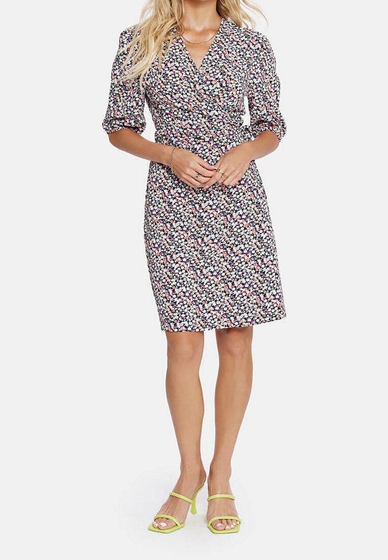 Blumenkleid mit dunklem Hintergrund und bunten Blüten, kurzen Puffärmeln und einer taillierten Silhouette, kombiniert mit grünen Riemchensandalen.