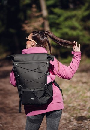 Schwarzer Rucksack mit Rolltop-Design, elastischen Kordelakzenten und Seitentasche, getragen von einer Person in einer pinken Jacke und grauen Leggings.