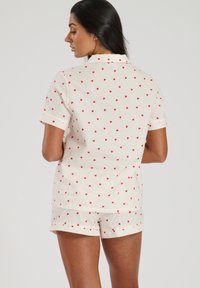 Ensemble de pyjama à manches courtes en coton écru avec un motif de cœurs rouges, comprenant un col et un short assorti avec des ourlets retroussés.