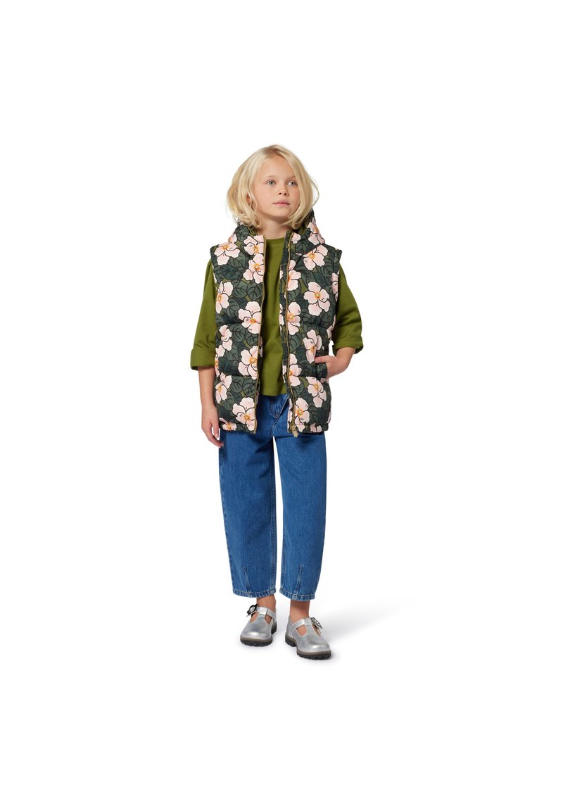 Kwietny kamizelka pikowana w ciemnozielonym kolorze z różowymi kwiatami, nałożona na zieloną bluzkę, w połączeniu z niebieskimi luźnymi dżinsami i srebrnymi butami.