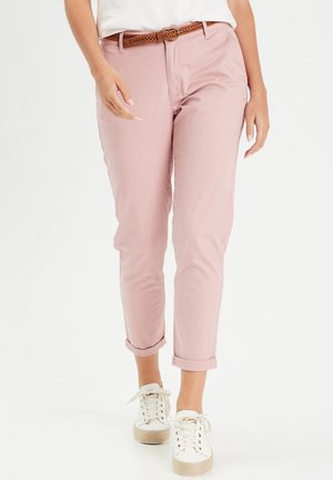 Personne portant un pantalon court rose clair avec une ceinture tressée marron et des baskets blanches à lacets marche en avant.