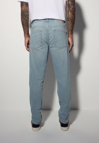 Jean en denim bleu clair avec une coupe droite, doté de poches arrière et d'une ceinture. Porté avec des baskets noires et blanches.