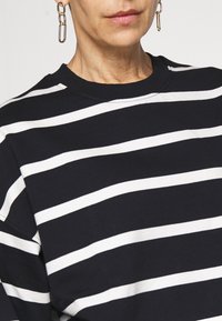 Sudadera a rayas en azul marino y blanco con cuello redondo, hecha de tela suave, con amplias rayas horizontales y un detalle de costura mínima.
