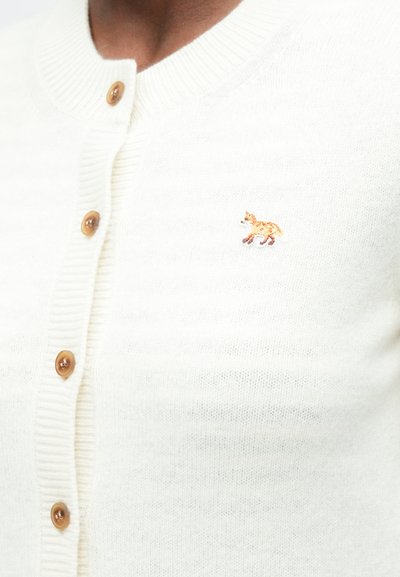 Cárdigan de punto blanco con cuatro botones marrones y un pequeño zorro naranja bordado en la parte izquierda del pecho.