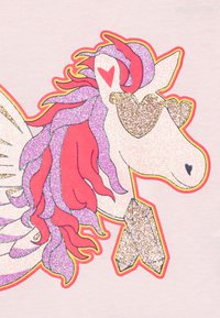 Graphisme de licorne avec des éléments scintillants roses, violets et dorés, de grandes ailes et des lunettes en forme de cœur sur un fond rose clair.