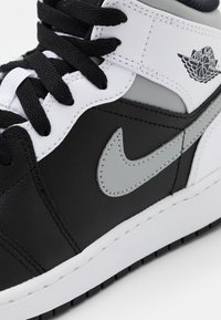 Fekete-fehér magas szárú sportcipő, amely bőrből készült, szürke Nike logóval, texturált talppal és fekete fűzővel rendelkezik.