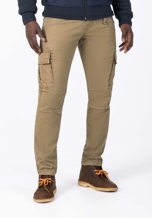 Khaki Cargo-Hosen mit Seitentaschen, aus einem Baumwollmischgewebe. Schmaler Schnitt, flacher Bund, kombiniert mit braunen Schnürstiefeln.