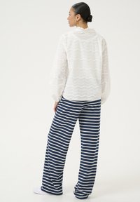 Blusa bianca testurizzata con motivi ondulati, abbinata a pantaloni larghi a righe blu navy e bianche. Design semplice, stile casual.