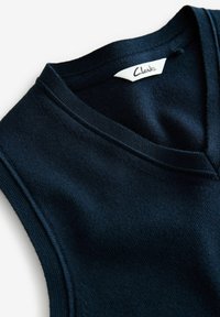 Tumedat sinine ilma varrukateta sviiter V-kaelusega, valmistatud pehmest, tekstureeritud kangast. Omab nähtavat silti, millel on kirjutatud "Clarks."