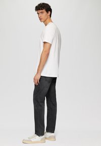 Witte katoenen T-shirt met korte mouwen, gecombineerd met donkergrijze slim-fit jeans en witte sneakers met crèmekleurige accenten. Eenvoudig ontwerp.