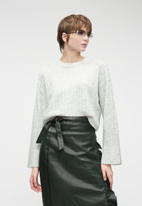 Light gray knitted sweater with a round neckline and dropped shoulders, paired with a dark green leather skirt featuring a tied belt detail.