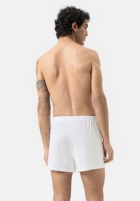 Boxers en coton blanc avec une ceinture élastique, présentant une texture lisse et un design simple et épuré, portés par une personne de dos.