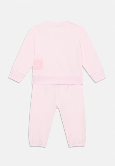 Rosa bomullsoverall med rund halsringning och långa ärmar. Har elastiska muddarna och en fyrkantig logotyp-patch på baksidan.