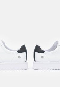 Sneaker bianchi in pelle con dettagli in pelle nera sul tallone, caratterizzate da un logo argentato vicino al tallone e una suola in gomma bianca.