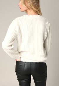 Pull blanc en maille côtelée, fabriqué dans un matériau doux, avec un col rond et des manches longues, associé à un pantalon en cuir noir bien ajusté.