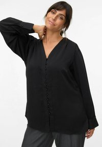 Blouse noire à manches longues avec un décolleté en V, fermeture à boutons sur le devant avec des boutons noirs, et un léger brillant. Tissu doux avec une coupe décontractée.