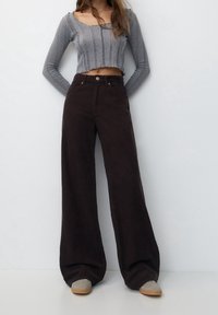 Afgekorte grijze ribbed trui gecombineerd met een brede bruine corduroy broek. Opvallende stiksels op de trui; de broek heeft voorzakken en een knoopsluiting.