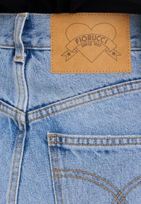 Džinsai su šviesiai mėlynu skalbimu, su oranžinėmis siuvimo detalėmis, odiniu ženkliuku, pažymėtu "Fiorucci since 1967", širdelės formos.
