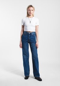 High-waisted, wide-leg blue denim jeans with a clean finish, paired with a fitted white short-sleeve crop top and black shoes.