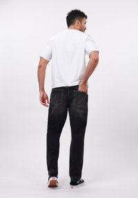 Vaqueros de mezclilla negros con un corte relajado, que presentan dos bolsillos traseros y costuras en contraste. Combinados con una camiseta de manga corta blanca lisa.