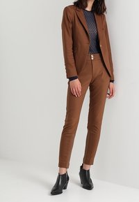 Brun skräddarsydd kavaj och matchande slim-fit byxor, kombinerat med en marinblå prickig topp och svarta klackstövletter.