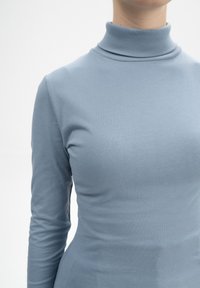 Hellblaues Rollkragenshirt aus weichem, dehnbarem Stoff. Verfügt über lange Ärmel und eine figurbetonte Silhouette. Glatte Textur, minimales Design.