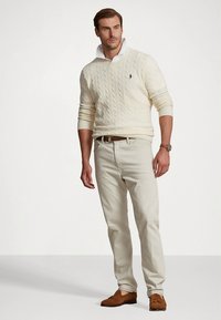 Εκρού πουλόβερ με πλεκτή υφή και ψηλό γιακά, συνδυασμένο με ανοιχτό μπεζ chino παντελόνια και καφέ μοκασίνια. Διαθέτει λογότυπο στο πουλόβερ.