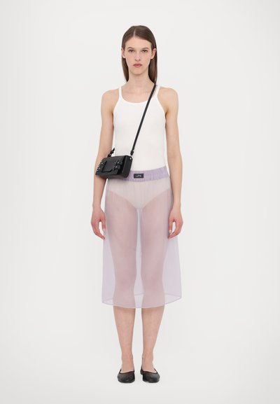 Un débardeur blanc, une jupe mi-transparent violet avec une taille élastique, et un sac bandoulière noir avec des accessoires décoratifs. Des chaussures plates noires.