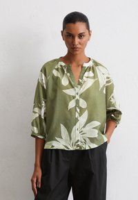 Green floral-patterned linen blouse with a button front, relaxed fit, and three-quarter sleeves. Features a round neckline and soft texture.
