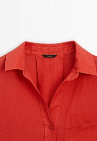 Chemise en lin rouge avec un col classique, une poche avant et des boutons. Le tissu présente une finition douce et texturée.