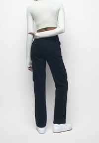 Pantalon cargo noir avec poches latérales, design à jambes droites et texture subtile. Associé à un crop top blanc ajusté à manches longues.