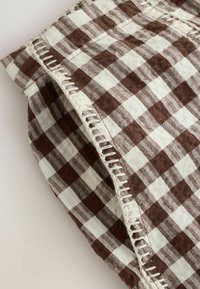 Tissu à carreaux marron et blanc avec couture en boucle blanche visible le long du bord plié sur une surface claire unie.