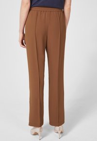 Bruna byxor med elastisk midja och rak benform, gjorda av ett mjukt tyg. Har rena linjer och en skräddarsydd look.