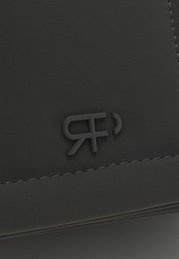Portafoglio in pelle nera con superficie texture, bordi cuciti e un logo in rilievo in tonalità scure per un design elegante.