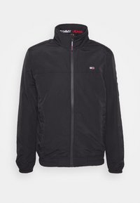 Svart zip-up jacka med hög krage, elastiska cuffs och nederkant, liten Tommy Jeans-logotyp på bröstet och märkt innerkrage.